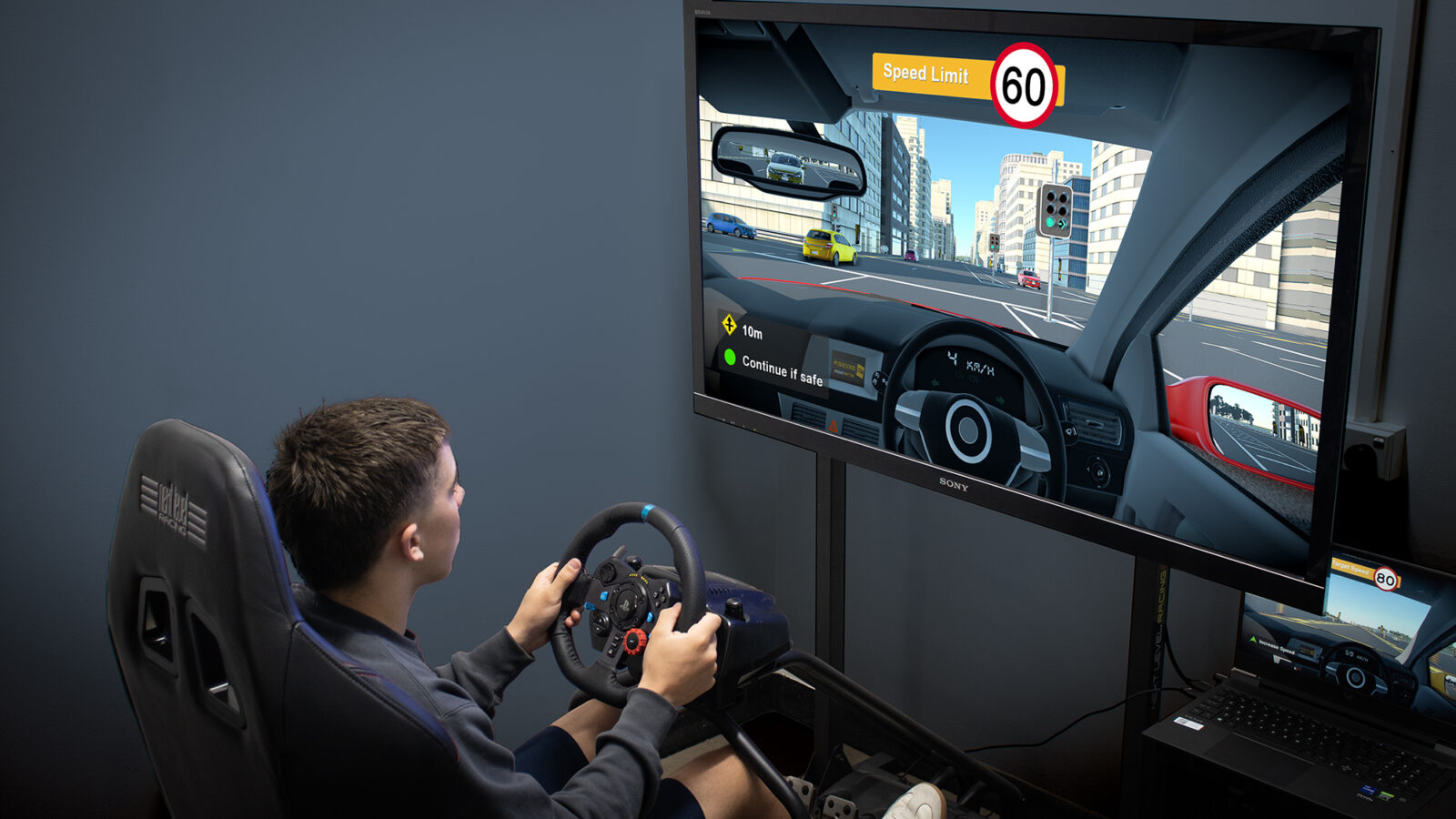 myDRIVESCHOOL in use — a wheel-and-pedal rig with the in-sim city driving view on screen